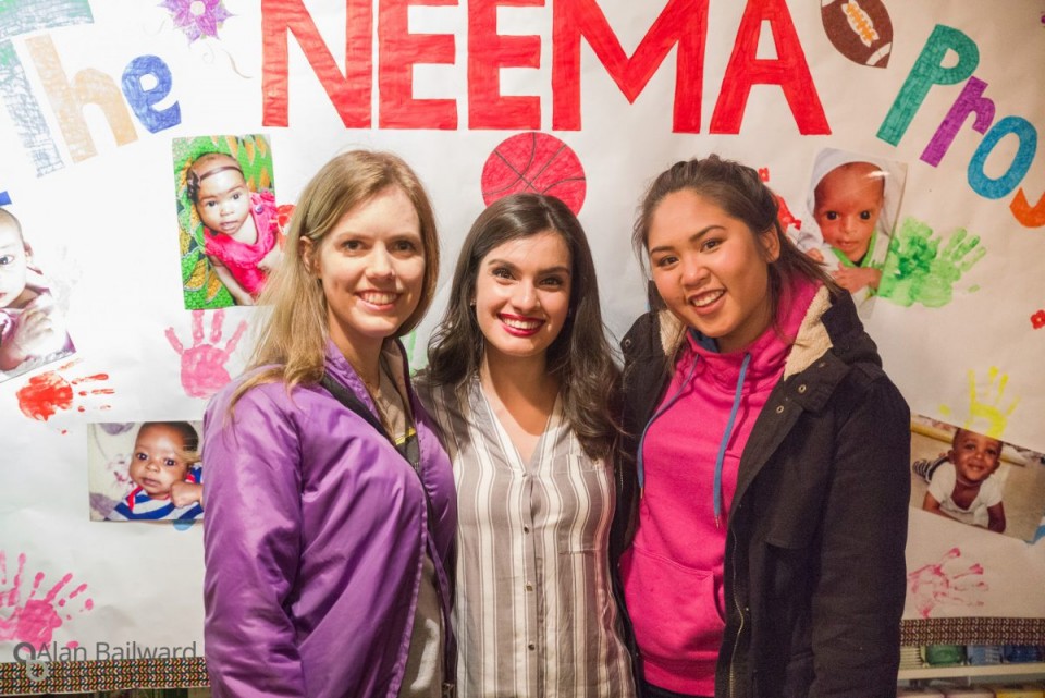 Three ladies in front of a NEEMA project poster